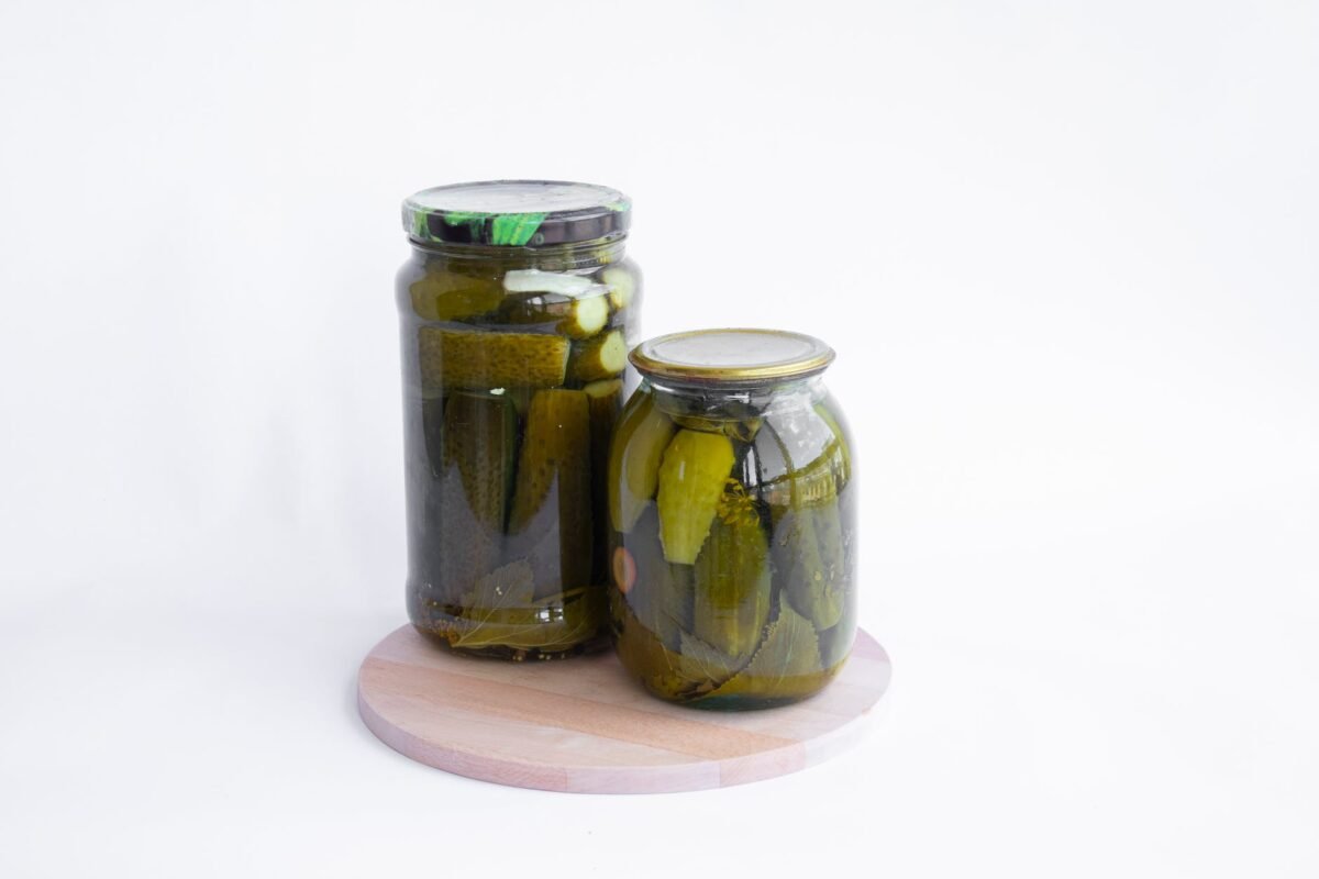 two clear glass jars of preserved pickles on a cutting board