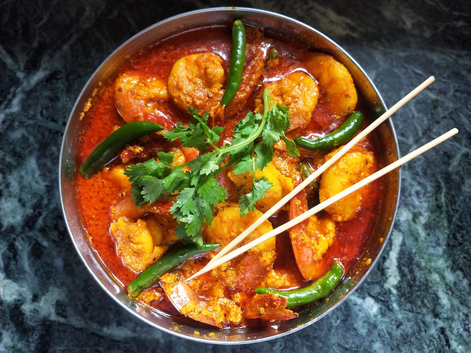 shrimps in sause with green chili peppers and parsley in round dish with chopsticks
